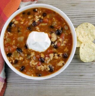 Looking down at a bowl of hearty black bean soup with scoop of sour cream on top.