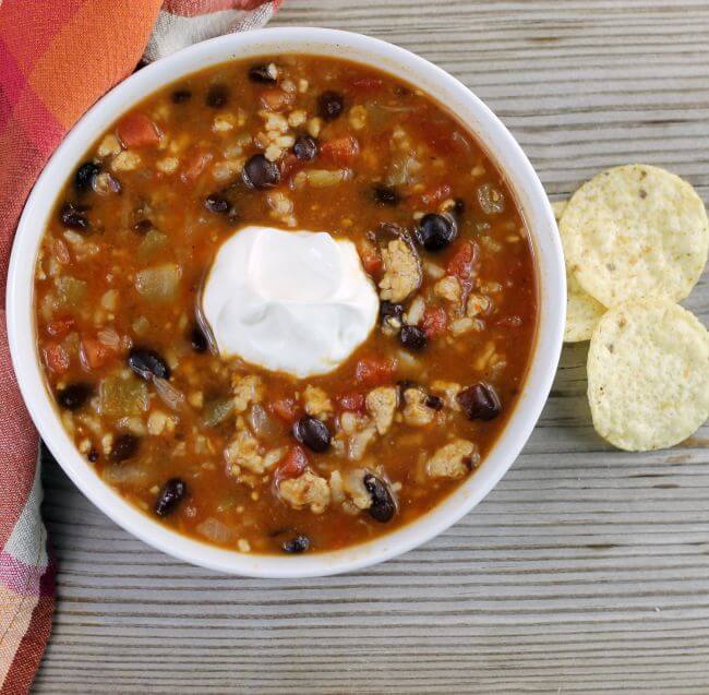 Looking down at a bowl of hearty black bean soup with scoop of sour cream on top. 