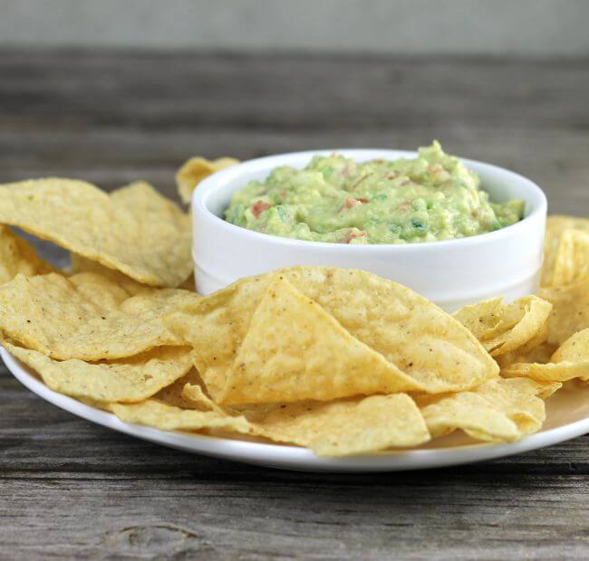 The dip in a white dish with chips on a plate.