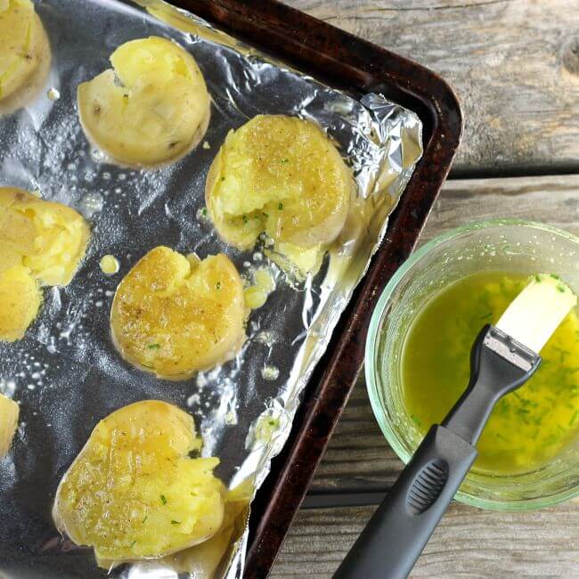 Smashed potatoes on a baking pan being brushed with a melted butter mixture.