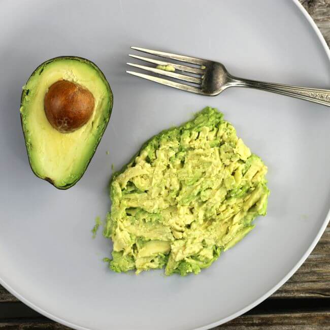 Mashing avocado with a fork on a gray plate.