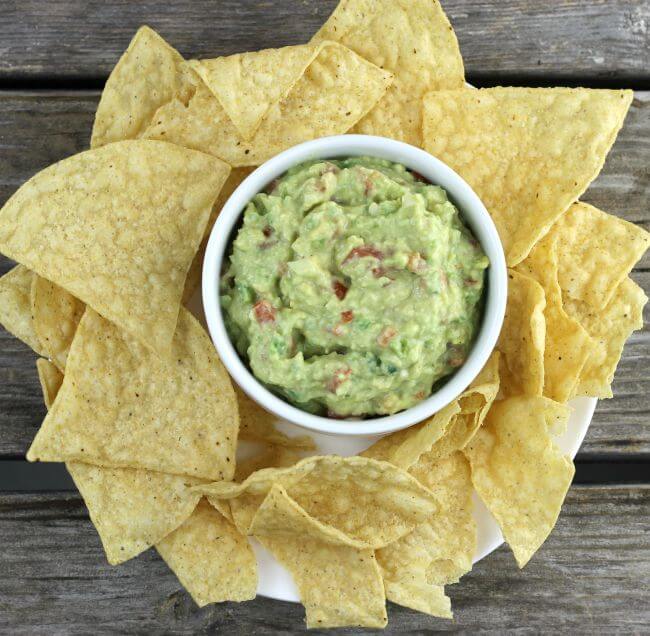 Guacamole in a white dish with tortella chips around the bowl.