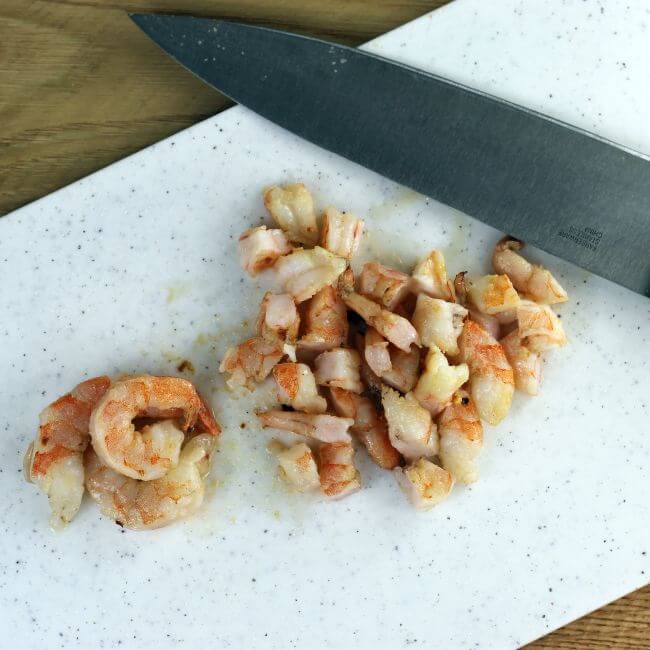 Cutting shrimp on a cutting board with a knife.