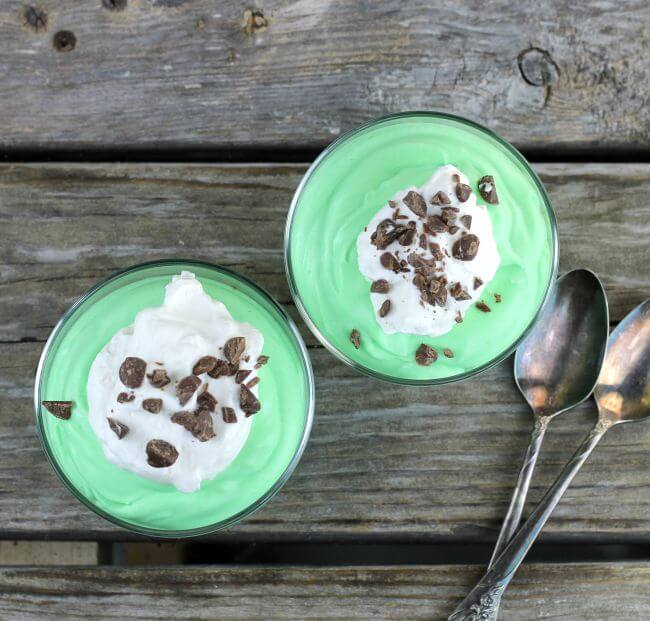 Looking down at 2 bowls of mint pudding with two spoons.