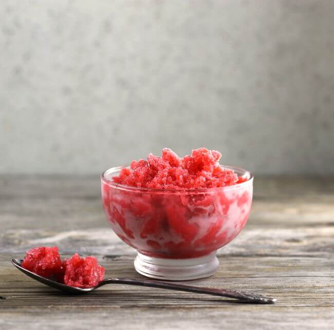 A side view of a bowl of strawberry Italina ice with a spoon in front.