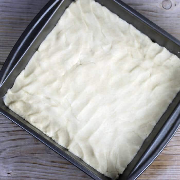 The dough is patted into the bottom of the baking pan.