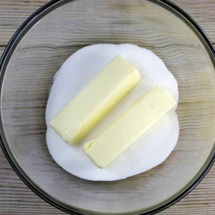 Two sticks of butter and sugar are added to a large bowl.