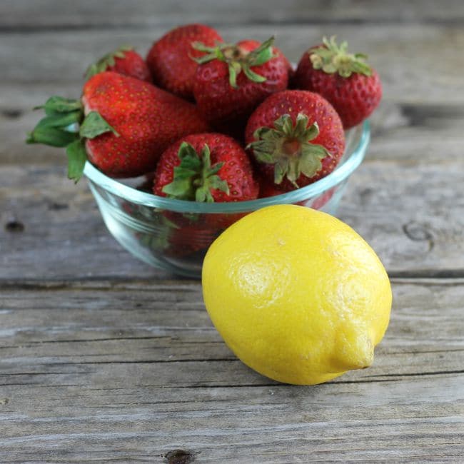 Stawberries in a bowl with a lemon in front.