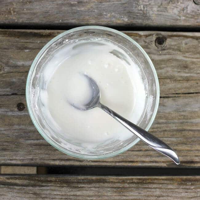 Lemon icing in a glass bowl with a spoon in the bowl.