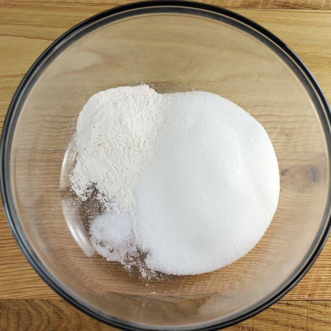 Sugar, flour, and salt are added to a glass mixing bowl.