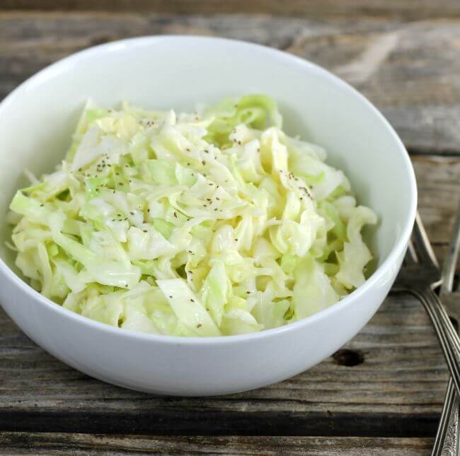 Coleslaw in a white bowl with forks on the side.