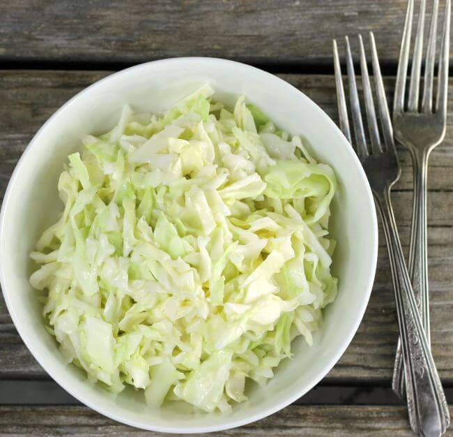 Overlooking a white bowl of coleslaw with forks on the side.