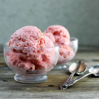 Two bowls of peach strawberry frozen yogurt with spoons on the side.