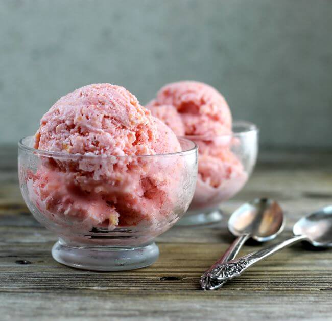 Two bowls of peach strawberry frozen yogurt with spoons on the side.