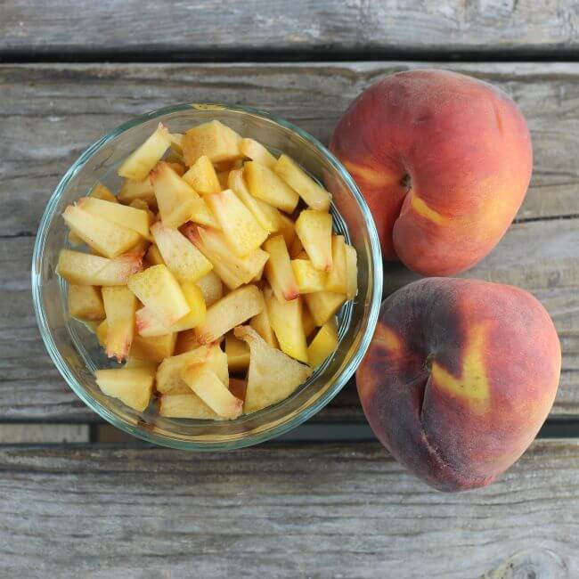 A peach cut into pieces with peaches on the side.