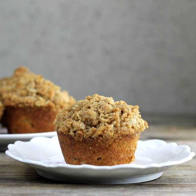 A side view of a muffin on a white plate with more muffins in the back.