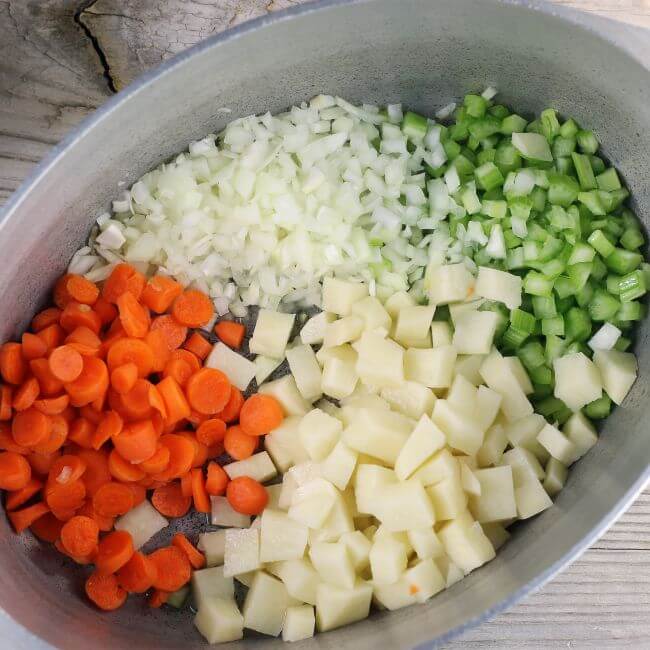 Chopped carrots, potatoes, onions, and celery in a Dutch oven.