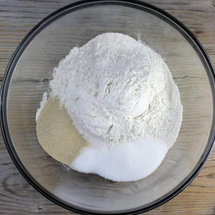 Flour, sugar, yeast, and salt are added to a large mixing bowl.