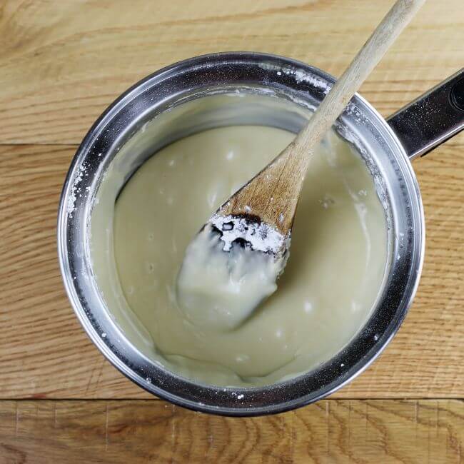 Brown butter frosting in a saucepan with a wooden spoon.