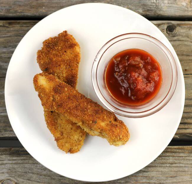 Looking down at taco chicken strips with a cup of salsa on a white plate.