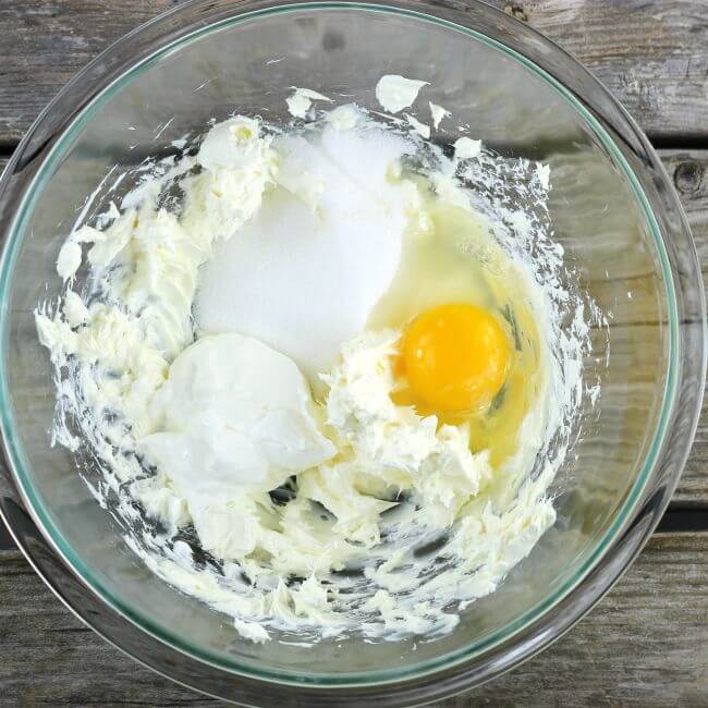 Cream cheese, sugar, sour cream, and a egg in a bowl.