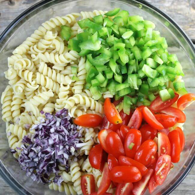 Red onion, green pepper, cherry tomatoes, and pasta in a bowl.
