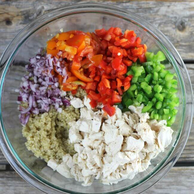 Onions, green pepper, red peppers, tomatoes, chicken, and quinoa in a bowl.