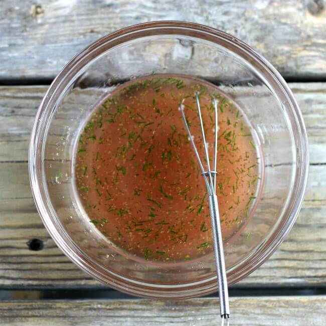 A bowl with the dressing for the salad with a whisk on the side of the bowl.