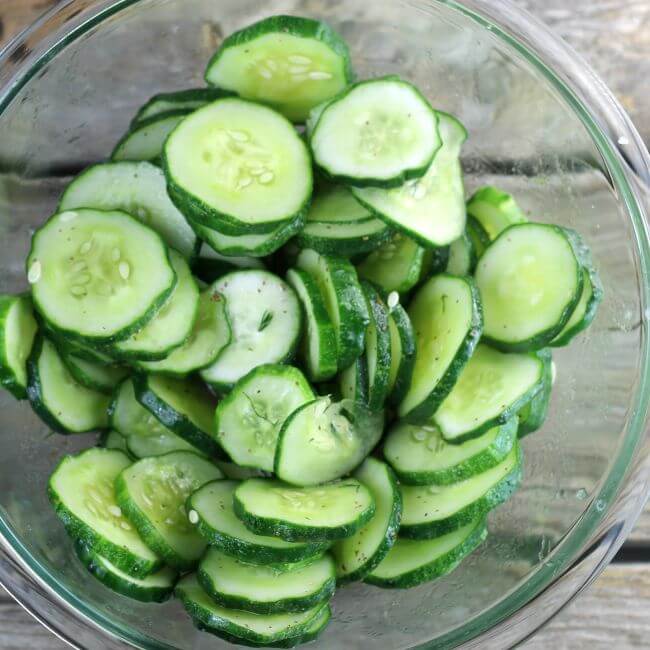 Sliced cucumbers in a glass bowl with vinegar dressing mixed in.