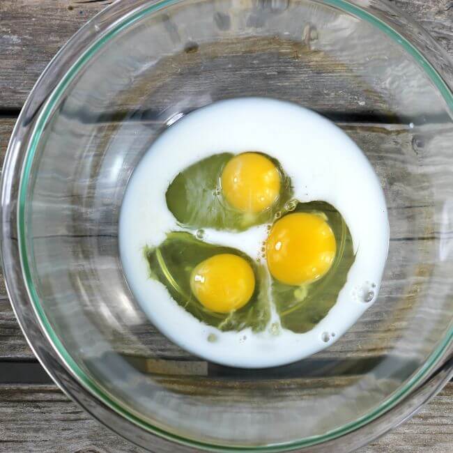 Three eggs and milk in a glass bowl.