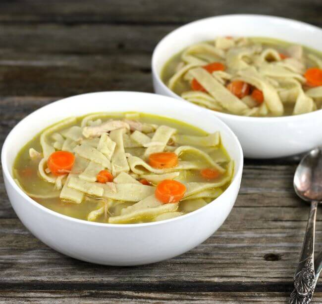 Side view of two bowls of chicken noodle soup.