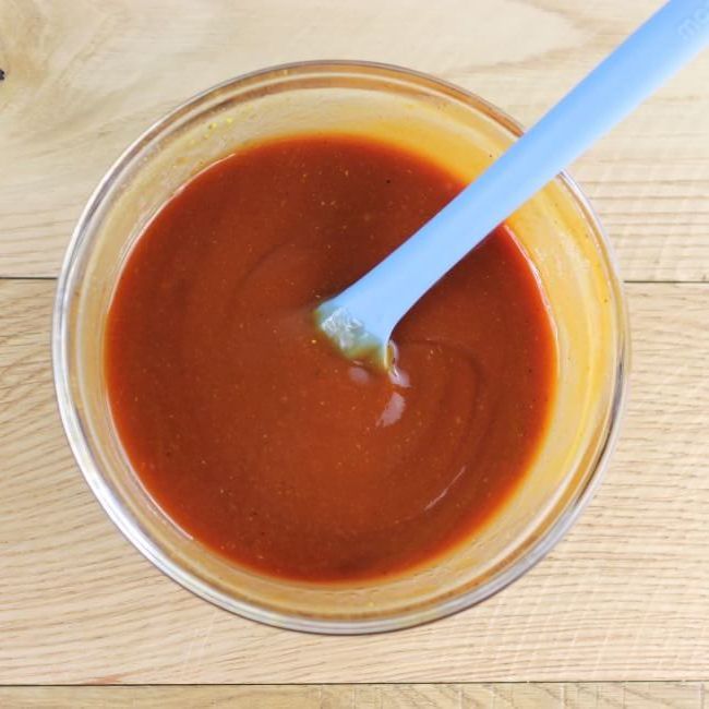 Homemade bbq sauce in a glass bowl with a blue spatula.