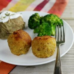 Close up view of meatballs in a white plate with a baked potato and broccoli.
