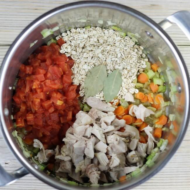 Diced tomatoes, barley, chicken, and bay leaves are added to the vegetables.