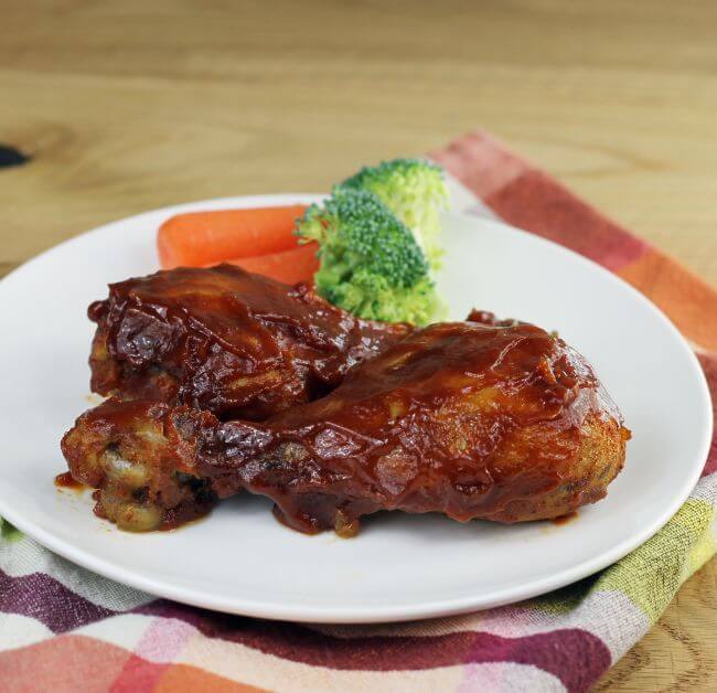 Side view of BBQ drumsticks on a white plate.
