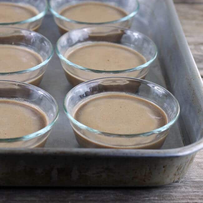 Custard cups filled with unbaked chocolate pudding in a baking pan.