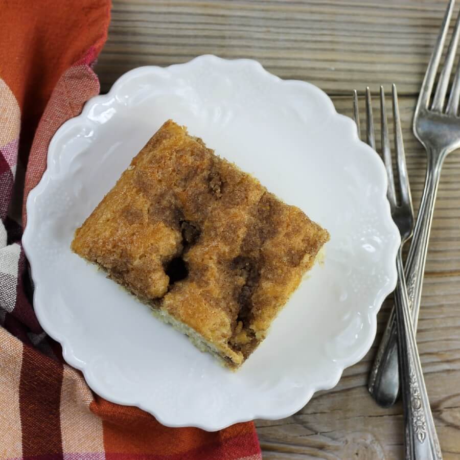 Over looking a piece of coffee cake on a white plate with forks on the side.