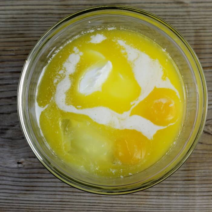 Eggs, melted butter, sour cream, and vanilla are added to a small mixing bowl.