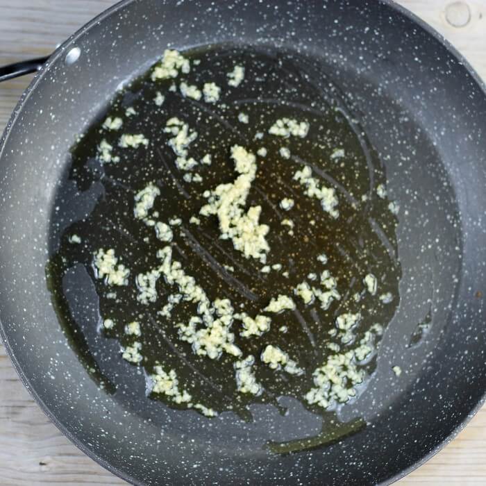 Olive oil and garlic are added to a large skillet. 
