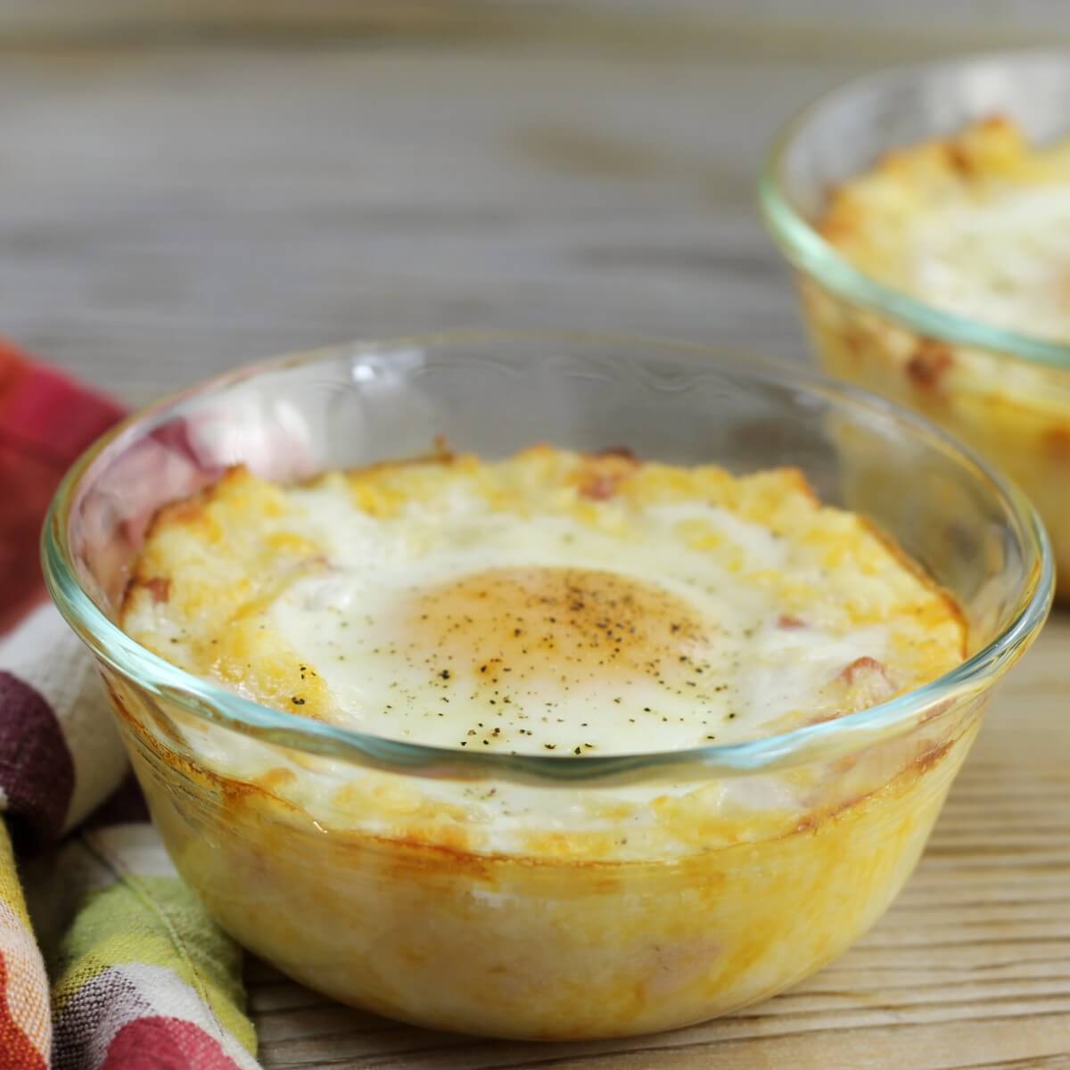 A side able of view of a bowl with baked mashed potatoes and an egg on top.