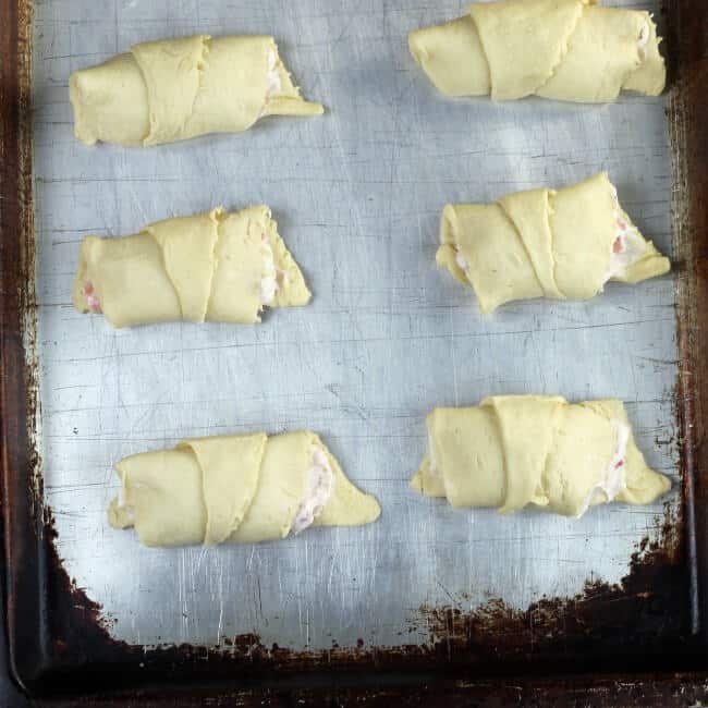 Filled crescent rolls on a baking sheet ready for the oven.