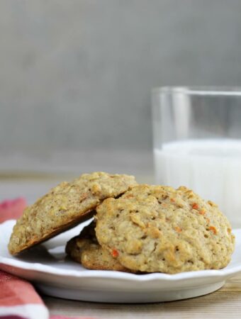 A side view of a plate of carrot apple cookies with a glass of milk.