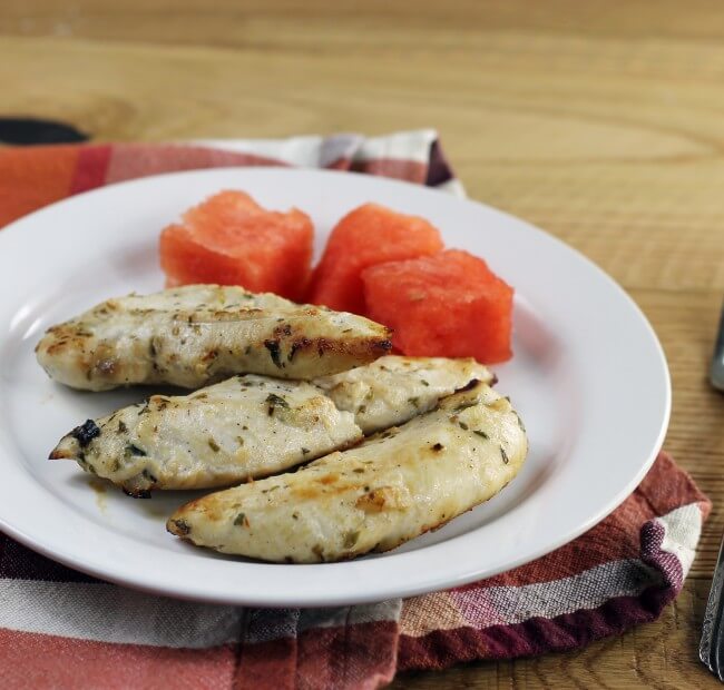 Chicken tenders with watermelon on a white plate.