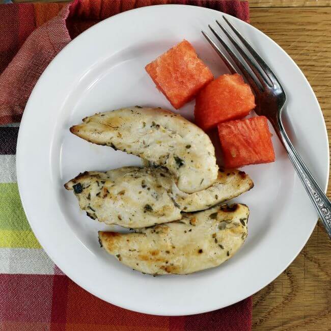 Over looking at a white plate with three simple broiled chicken tenders. 