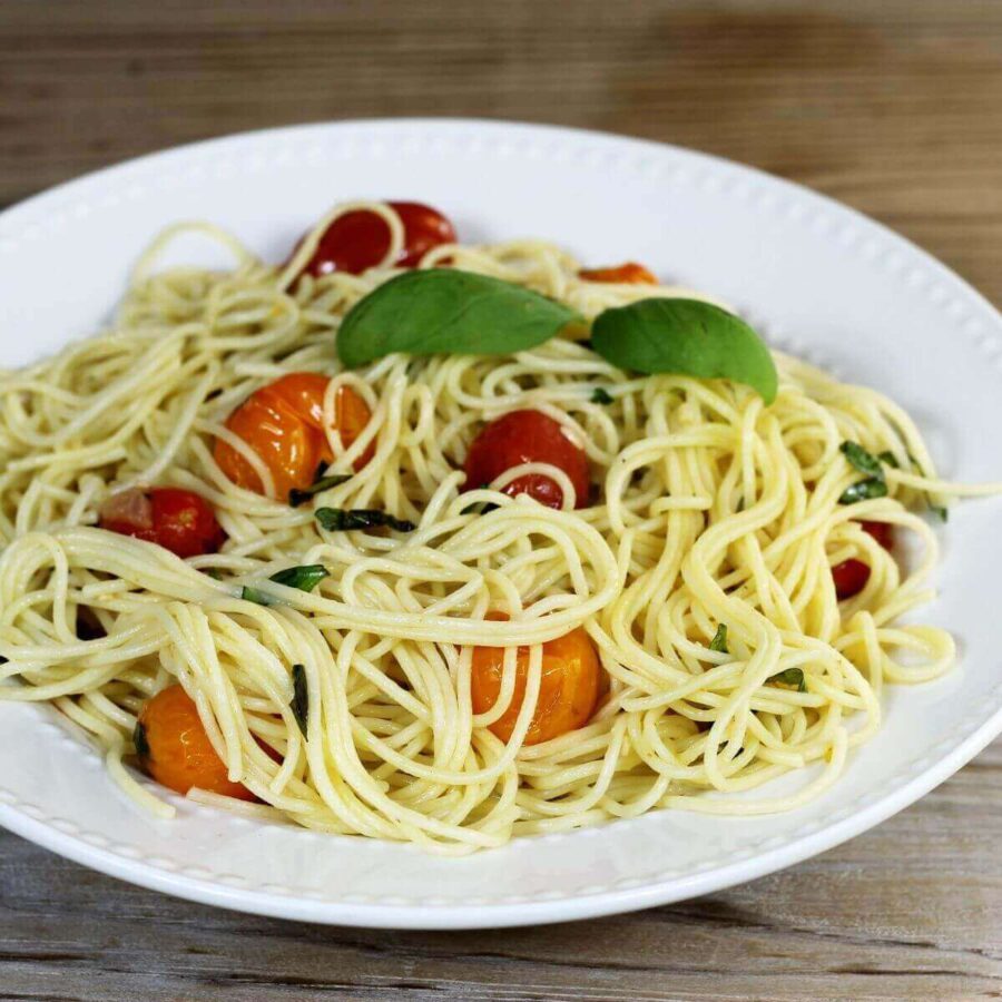 View of a side angle view of a plate of pasta with cherry tomatoes.