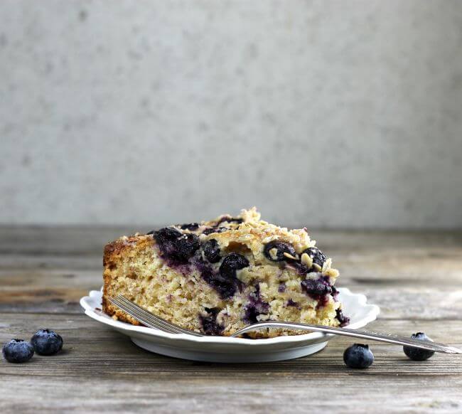 Side view of blueberry cake with a fork on a white plate.