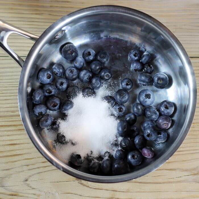 Blueberries and sugar added to a small saucepan.