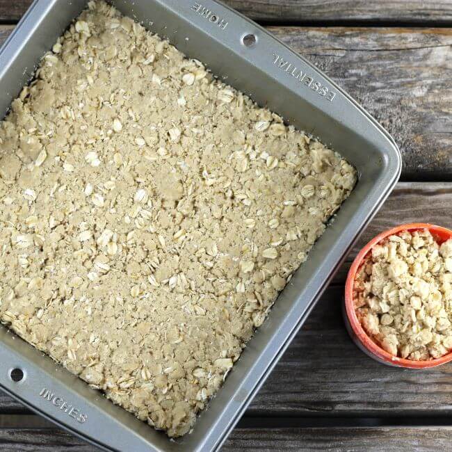 Crust in a baking pan with a measuring cup of crumble