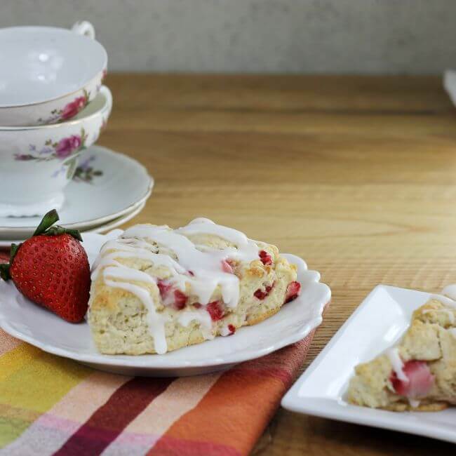 Side view of scones on white plates with tea cups in the back.