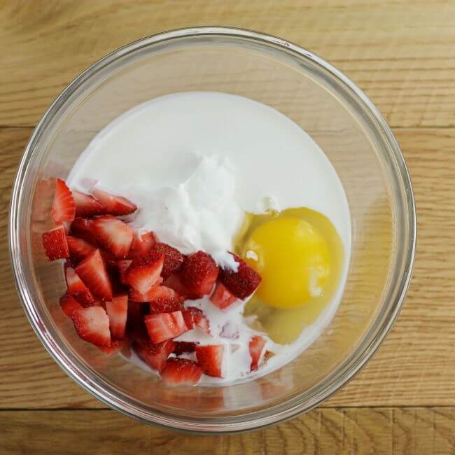 Looking down at a bowl of strawberry, an egg, sour cream, and egg.